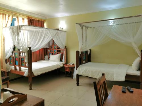 New Safari Hotel的一间卧室设有两张天蓬床、一张桌子和一张桌子。