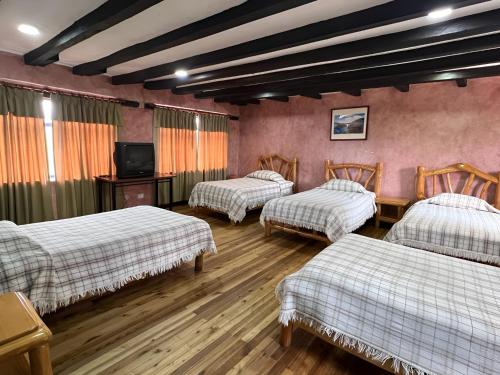 SaraguroHotel Achik Wasi的客房设有三张床、一张桌子和一台电视。