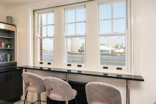 伦敦3 x Bedroom Riverside Flat with Beach的客房设有三扇窗户和一张桌子及椅子。