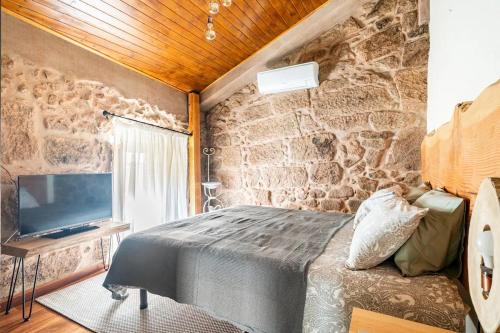曼瓜尔迪Segredos da Montanha - Mangualde的一间卧室设有石墙、一张床和电视。