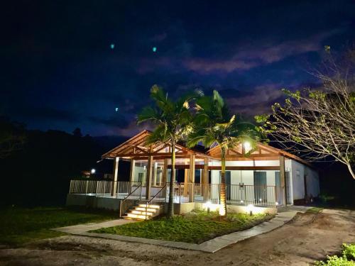 佩德拉阿祖尔Pousada Rural Recanto do Lago的一座晚上有门廊和棕榈树的房子