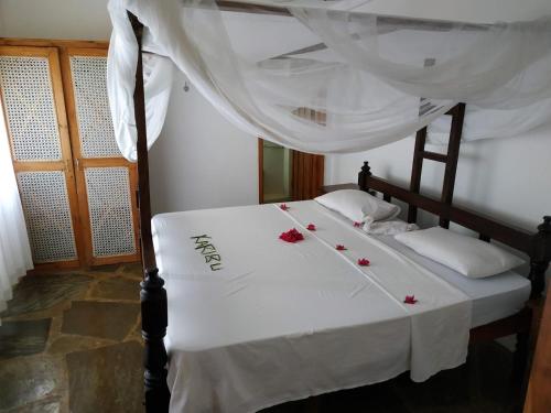 马林迪Silver Rock Hotel的一张床上铺有白色床单和红色玫瑰