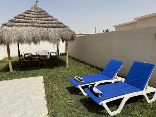 DjerbaSuperbe villa avec piscine sans aucun vis à vis的两张蓝色的椅子、一张桌子和一把草伞