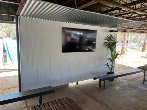 艾利斯斯普林斯Heritage Caravan Park的白色的墙壁,有两把长椅和一台电视机