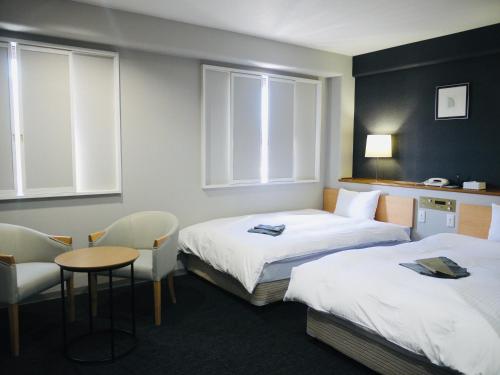 伊万里市伊万里中央酒店 的酒店客房带两张床和一张桌子以及椅子。