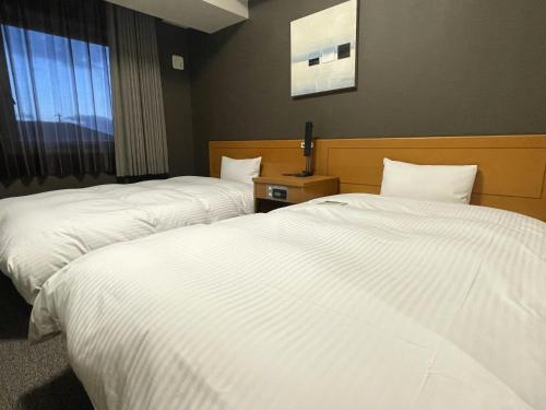 御前崎市御前崎鲁特因酒店的配有白色床单的酒店客房内的两张床