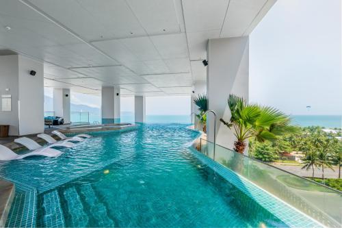 岘港Awaken Da Nang Hotel的一座带椅子和大海的酒店中的无边游泳池