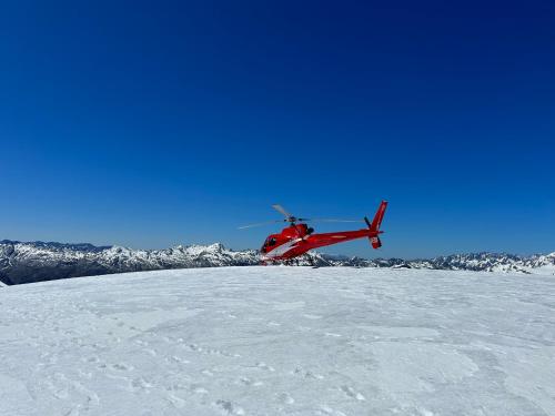 霍基蒂卡Drifting Sands Beachfront Retreat的一架红色直升机飞越雪覆盖的山