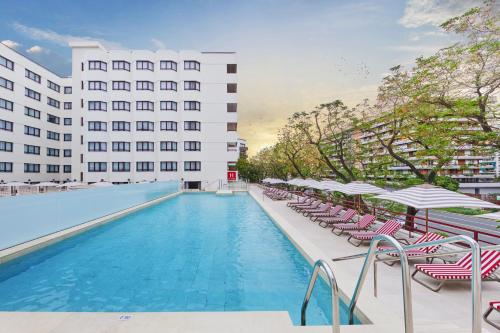 塞维利亚塞维利亚赫斯珀里亚酒店的一座带椅子和遮阳伞的游泳池位于一座建筑旁边