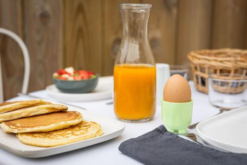 梅里尼亚克Chambres d'hôtes Le Studio Bordelais avec bain nordique的一张桌子,上面放着煎饼和鸡蛋,还有一瓶橙汁