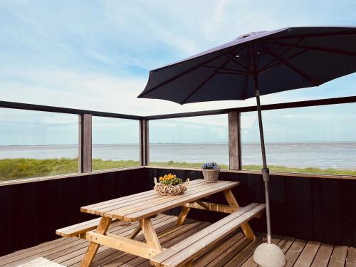 WesterlandChalet direct aan Waddenzee的甲板上配有遮阳伞的野餐桌