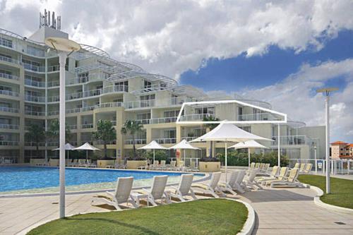 艾塔龙海滩Ettalong Beach Luxury Apartments的一座大建筑前的带椅子和遮阳伞的游泳池