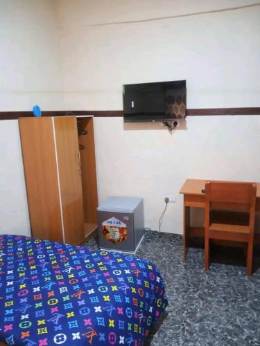 伊巴丹AMIGOS HOTEL的一间卧室配有一张床、一张书桌和一台电视。