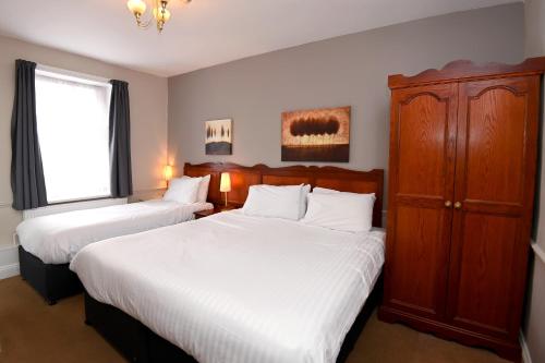 灵伍德Original White Hart, Ringwood by Marston's Inns的一间卧室设有两张床、一个橱柜和一个窗口。