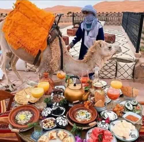 梅尔祖卡Desert Berber Camp的骆驼和一位站在餐桌旁的女人
