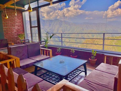 穆索里The Pine Woods - A Four Star Luxury Resort in Mussoorie的客房设有桌椅和大窗户。