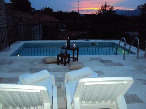 格鲁达Villa Petrosa的游泳池畔的两把白色椅子和一张桌子