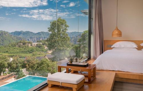 张家界Avatar Mountain Resort的一间卧室设有一张床和一个带游泳池的大窗户