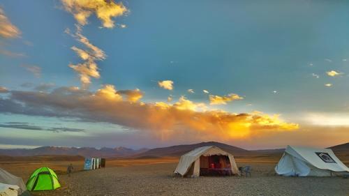 锡卡都Mantri Bai Camping Site Deosai的一群在沙漠中的帐篷,在天空中有一根彩虹