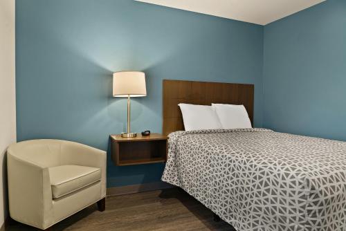 迈尔斯堡WoodSpring Suites Fort Myers - Cape Coral的一间卧室配有一张床、一把椅子和一盏灯
