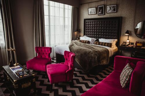 曼彻斯特哥谭酒店的一间卧室配有一张大床和两张粉红色的椅子