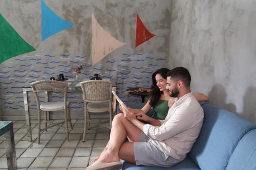 马塞约Pousada Praia Pajuçara的坐在沙发上读书的男人和女人