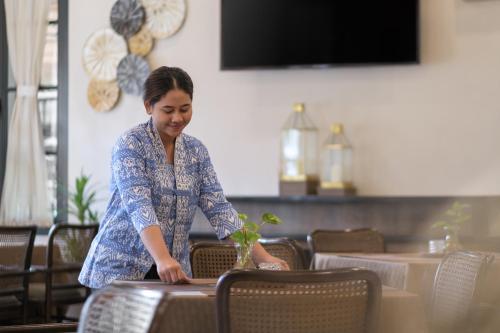 日惹The Margaux Hotel Yogyakarta的女人坐在桌子上,一边种植物