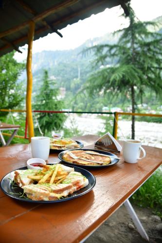 马拉里Himtrek River Side Camps and Hostel Manali的一张木桌,上面放着食物盘