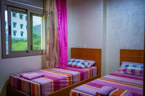 Akchourhotel el amri akchour的配有粉红色窗帘的客房内的两张床