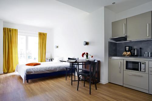 汉堡Apartmenthaus Hamburg Les Jardins的一间卧室配有一张床铺和一张桌子,还设有一间厨房