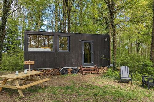SonchampTiny House La Clairière au milieu des bois !的树林里的一个黑色小房子,带一张野餐桌