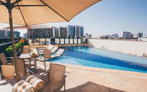 巴西利亚Cullinan Hplus Premium Flat Vip的一座带椅子和遮阳伞的建筑屋顶游泳池