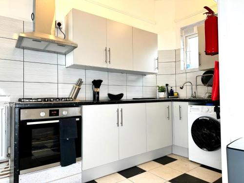 伦敦Serviced 4 bed 2 bath Manor Park House的厨房配有白色橱柜和黑烤箱。