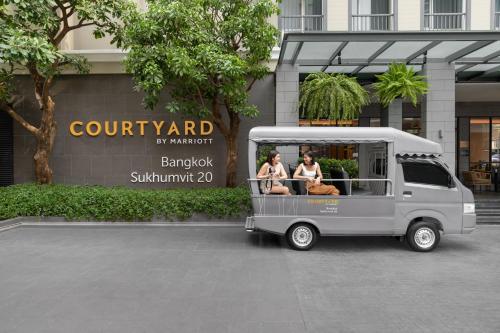 曼谷 曼谷素坤逸20号万怡酒店的两个女人坐在一辆面包车前,在一幢楼房前