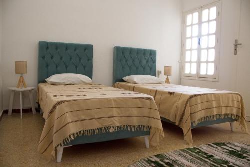 GabèsBEAU SÉJOUR hébergement et spa的一间卧室设有两张带蓝色床头板的床和窗户。
