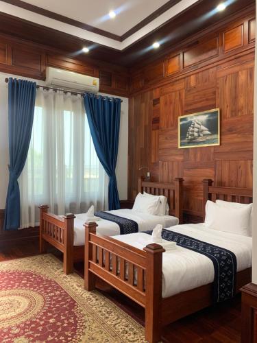 沙湾拿吉HotelLaoMixay的配有木墙和蓝色窗帘的客房内的两张床