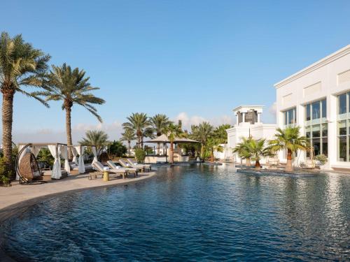 麦纳麦Raffles Al Areen Palace Bahrain的棕榈树度假村的游泳池以及大楼