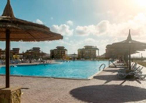 阿莱曼Blumar Sidi Abdel Rahman 2 bedrooms Chalet North Coast的一个带遮阳伞的大型游泳池以及部分建筑