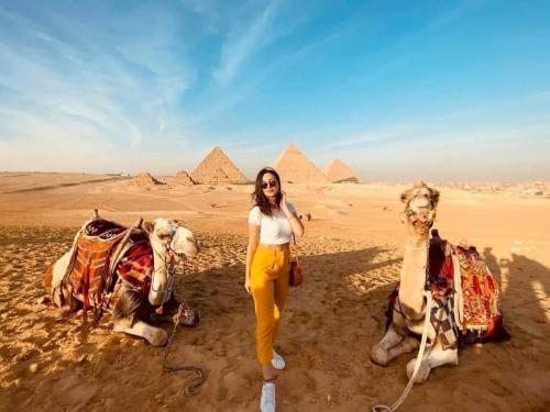 开罗Pyramids Express View HoTeL的金字塔上两个骆驼旁边站着的女人