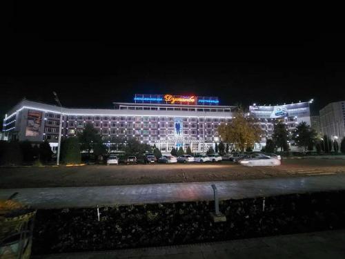 杜尚别Dushanbe Hotel的一座有照明的建筑,里面的汽车停在停车场
