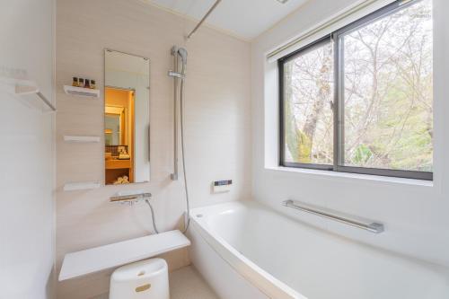 Izumi樱泉会馆的白色的浴室设有浴缸和窗户。