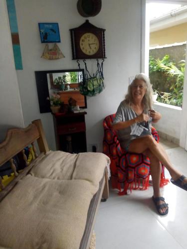 大普拉亚Xixova Hostel Japui são Vicente的坐在带时钟的房间里椅子上的女人