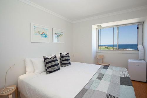 悉尼Ocean view Clovelly的一间白色的卧室,配有一张享有海景的床