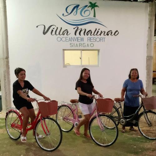 BurgosVilla Malinao Oceanview Resort - Deluxe bungalow的站在自行车旁的四个妇女站在一个标志前
