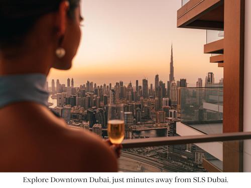 迪拜SLS Dubai Hotel & Residences的一位拿着一杯葡萄酒的女人,看着城市