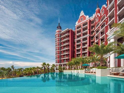 潘切Mövenpick Resort Phan Thiet的一座红色大建筑前的游泳池