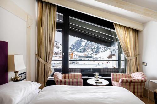 祖尔斯A-ROSA Collection Hotel Thurnher's Alpenhof的酒店客房设有一张床、两把椅子和一扇窗户。