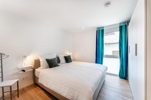施卢赫湖Luxuswohnung Traumblick - Neubau 2023的一间卧室配有白色的床、蓝色窗帘和窗户