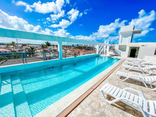 蓬塔卡纳DELUXE SUITES STUDIOS DUCASSI Sol Caribe HOTEL Bavaro WIFI Parking BBQ Beach CLUB & SPA的一座带白色椅子的建筑屋顶上的游泳池