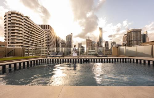 悉尼Accommodation Sydney City Centre 1 Bedroom Apartment with Balcony的一位女士在一座带游泳池的建筑的屋顶上行走